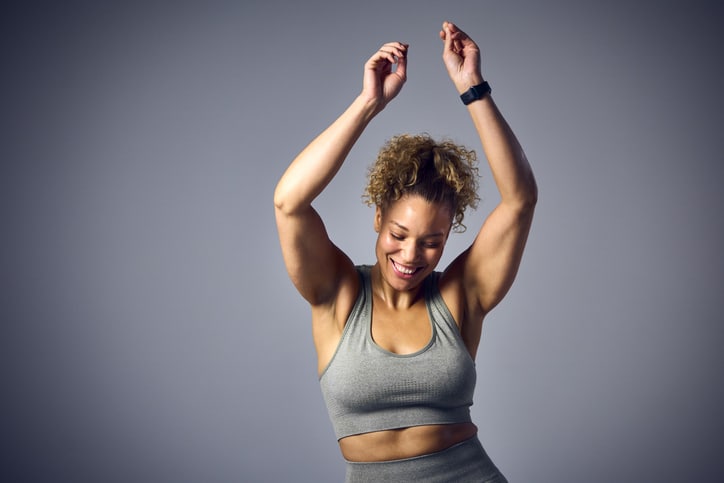 Studio Shot Of Woman Wearing Gym Fitness Clothing Dancing In Zumba Class On Grey Background